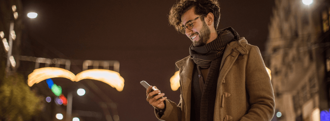 Glimlachende man in de stad die op zijn telefoon kijkt
