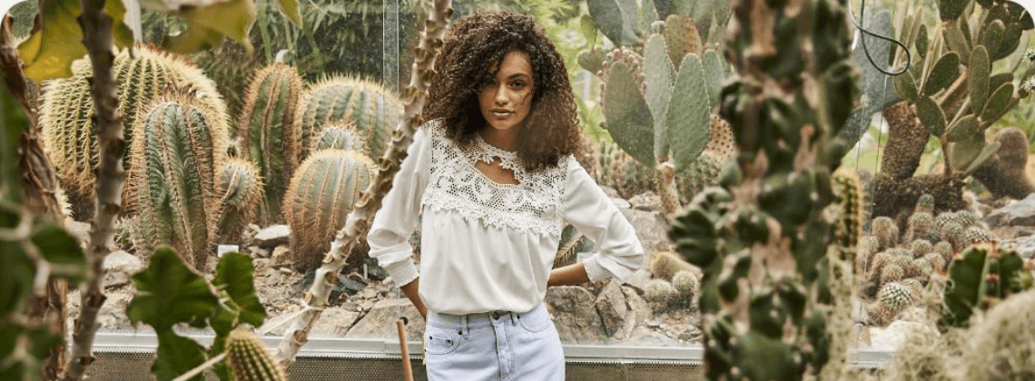 Vrouw met wit topje en spijkerbroek tussen de cactussen