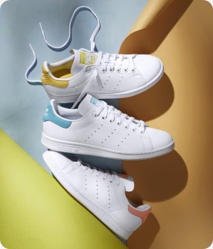 Drie Adidas schoenen liggend op een gekleurde grond