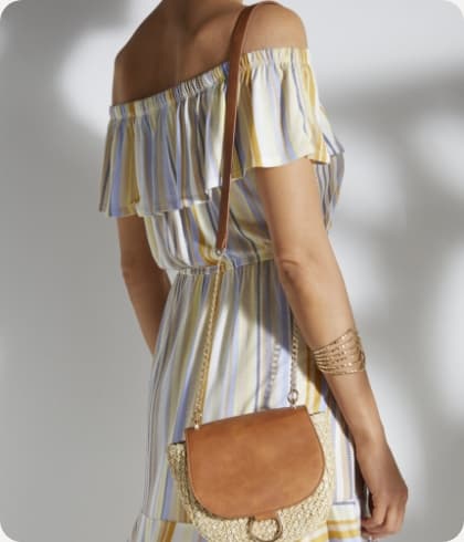 Vrouw met een kleurrijke jurk aan een tasje hangt over haar schouder en ze heeft gouden armbanden om