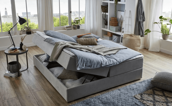 Slaapkamer met boxspring in het midden waarvan de helft open staat om spullen op te bergen