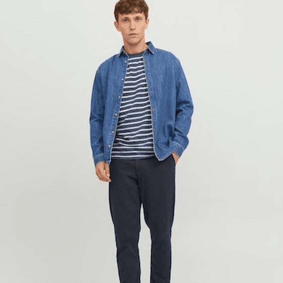 Een man met een gestreept shirt, spijkerjasje en een donkerblauwe chino aan