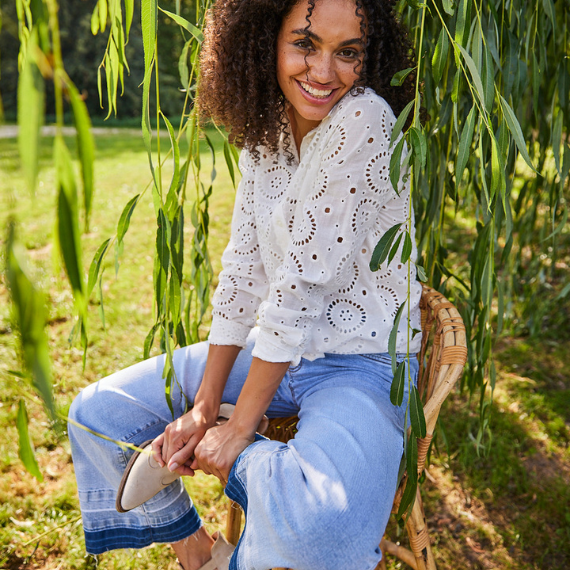 Vrouw met blauwe flared jeans en een wit blouseje op een stoel in de natuur