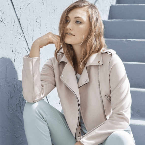 Vrouw die op de trap zit met pastel blauwe broek en een pastel roze jasje aan