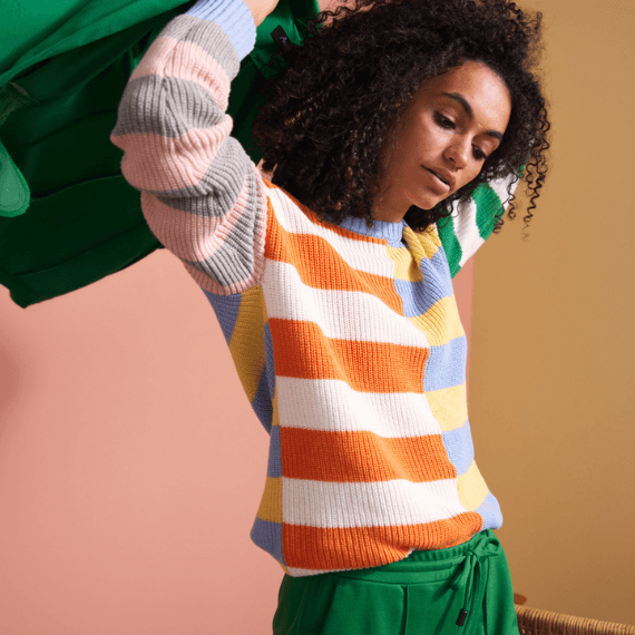 Vrouw met groene broek en gekleurde trui die groene blazer aantrekt