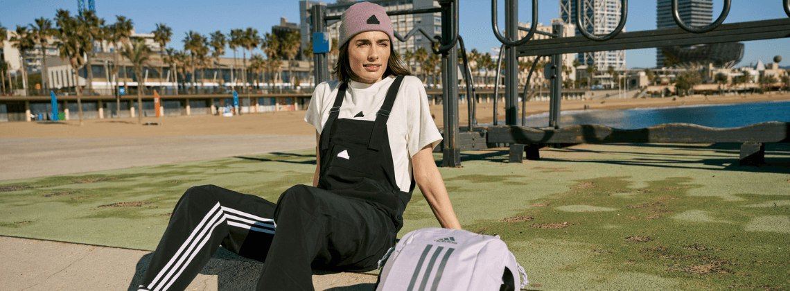 Vrouw buiten in een speeltuintje met een Adidas tuinbroek aan en een Adidas tas naast haar