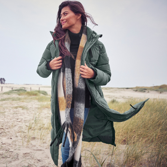 Vrouw op het strand met een groene gewatteerde jas aan