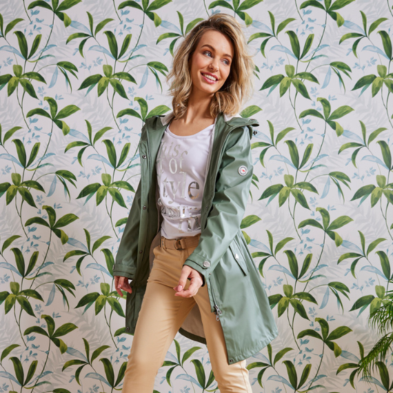 Vrouw voor een behangen muur met een groene zomerjas aan