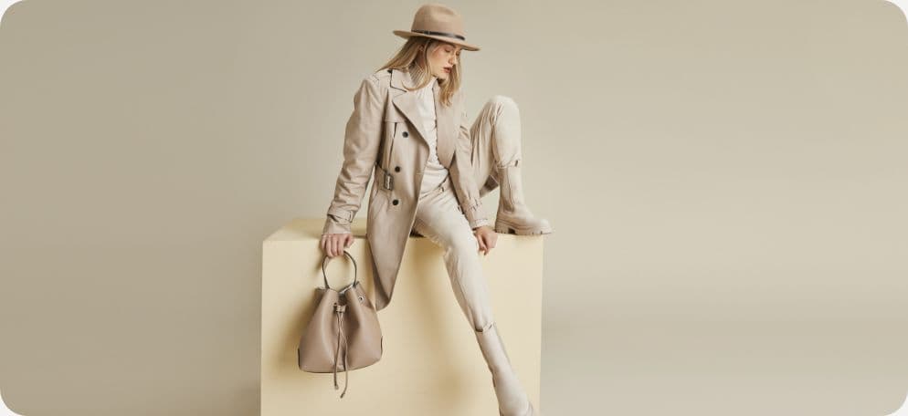 Vrouw helemaal gekleed in beige met een hoed en een tas zittend op een beige blok